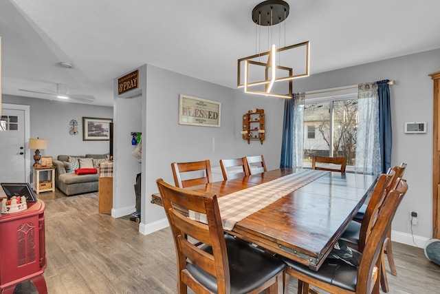 dining space featuring ceiling fan with notable chandelier, wood finished floors, and baseboards