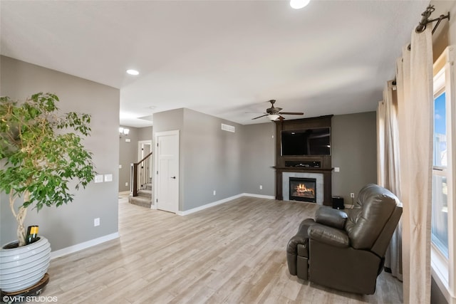 living room featuring stairs, light wood-type flooring, a tiled fireplace, and baseboards