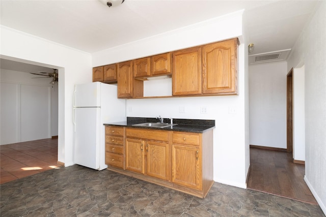 kitchen featuring visible vents, ornamental molding, brown cabinets, freestanding refrigerator, and a sink