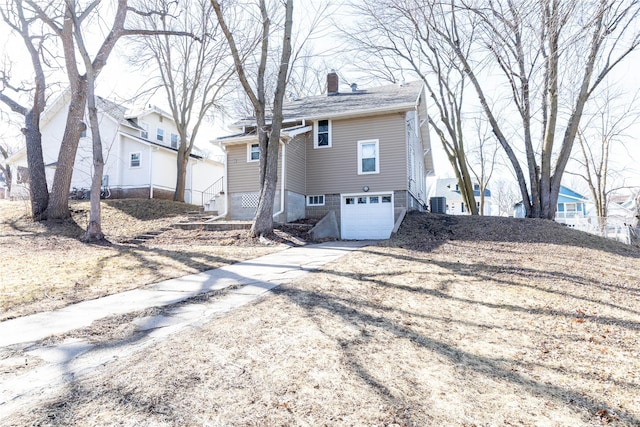 rear view of property featuring a garage, driveway, and a chimney