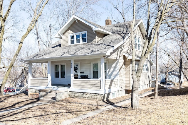 view of front facade featuring a porch, a chimney, and a shingled roof