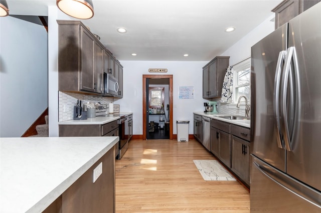 kitchen featuring stainless steel appliances, a sink, light wood-style flooring, and dark brown cabinets