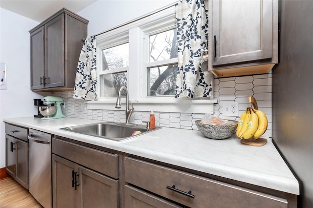 kitchen with light countertops, stainless steel dishwasher, a sink, and decorative backsplash