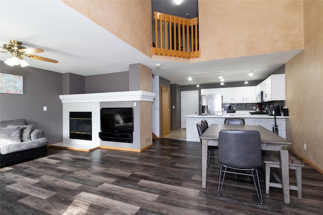 interior space featuring dark wood-style floors, stainless steel refrigerator with ice dispenser, a glass covered fireplace, open floor plan, and white cabinetry