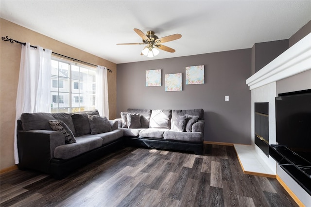 living area featuring a tiled fireplace, wood finished floors, a ceiling fan, and baseboards