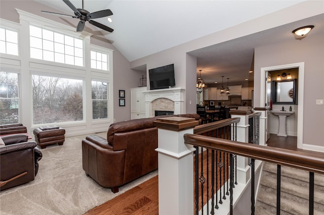 living area with light wood finished floors, baseboards, a glass covered fireplace, high vaulted ceiling, and ceiling fan with notable chandelier