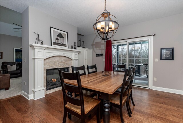 dining space with a chandelier, a stone fireplace, baseboards, and wood finished floors