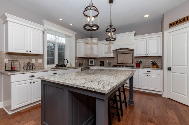 kitchen with a breakfast bar area, a sink, white cabinetry, custom exhaust hood, and dark wood finished floors