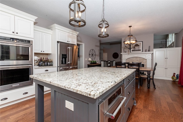 kitchen with dark wood-style flooring, decorative light fixtures, a fireplace, appliances with stainless steel finishes, and white cabinets