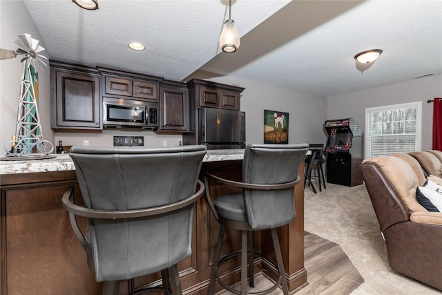 kitchen with visible vents, open floor plan, fridge, stainless steel microwave, and a kitchen bar