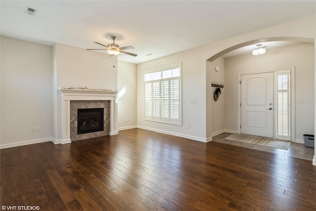 unfurnished living room with arched walkways, dark wood-type flooring, a fireplace, and baseboards