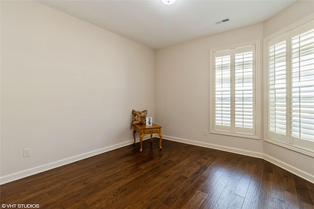 empty room with dark wood-style flooring, visible vents, and baseboards