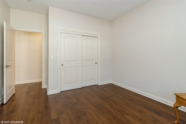 unfurnished bedroom featuring a closet, dark wood-style flooring, and baseboards