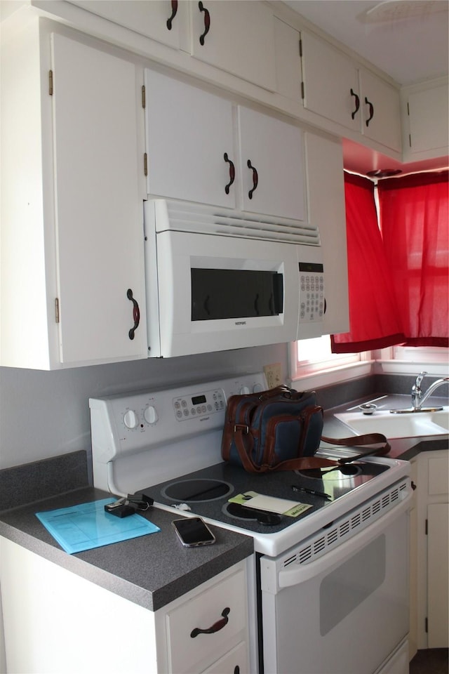 kitchen featuring dark countertops, white appliances, and white cabinetry