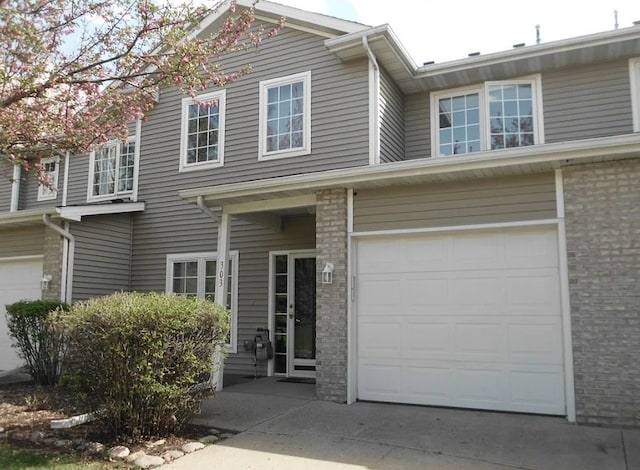 view of property with an attached garage, concrete driveway, and brick siding