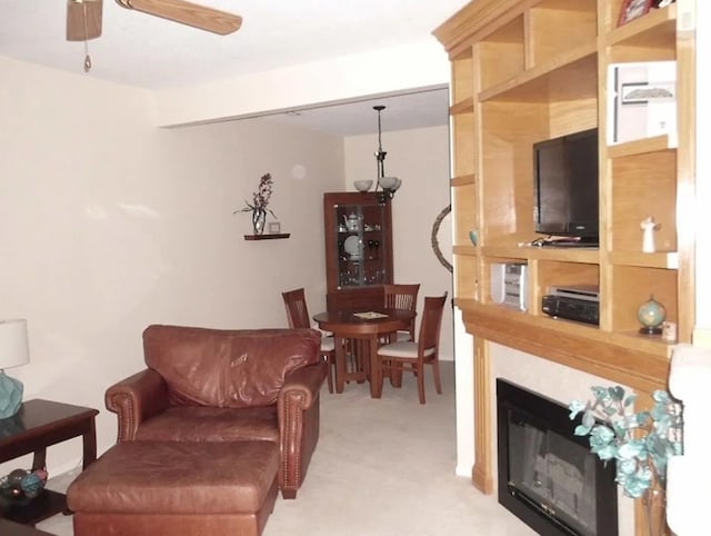 living area with light carpet, a glass covered fireplace, and a ceiling fan