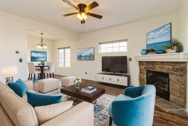 living area with ceiling fan with notable chandelier, a stone fireplace, and wood finished floors