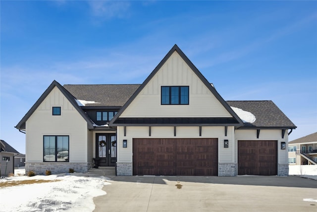 modern farmhouse style home with a shingled roof, stone siding, french doors, driveway, and board and batten siding