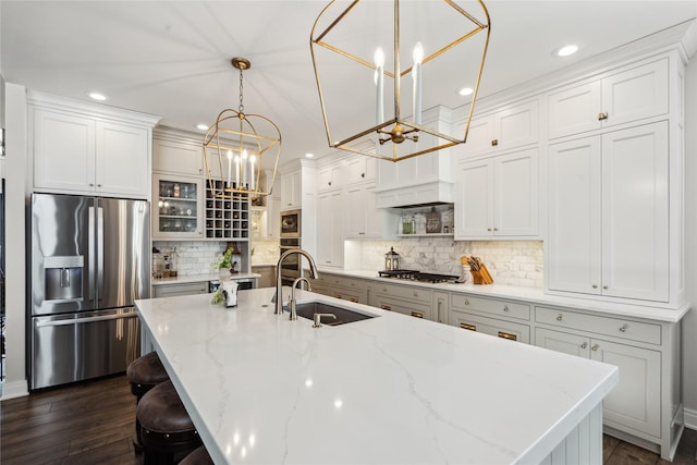 kitchen featuring a center island with sink, dark wood-style floors, a sink, stainless steel appliances, and a notable chandelier