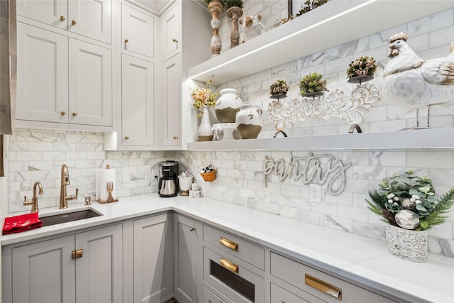 kitchen with white cabinets, light stone counters, backsplash, and a sink