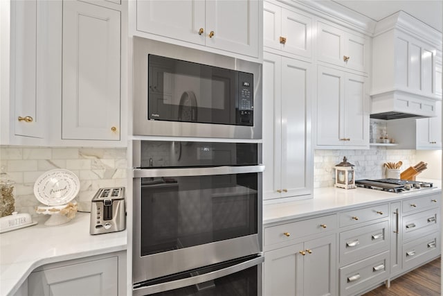 kitchen with appliances with stainless steel finishes, white cabinets, dark wood finished floors, and tasteful backsplash