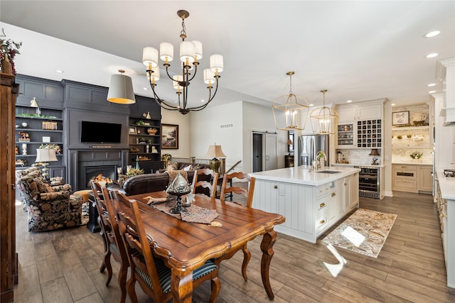 dining space with wine cooler, wood finished floors, a lit fireplace, and an inviting chandelier