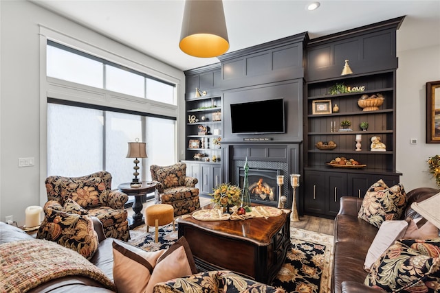 living room featuring a lit fireplace, built in shelves, and light wood-style floors