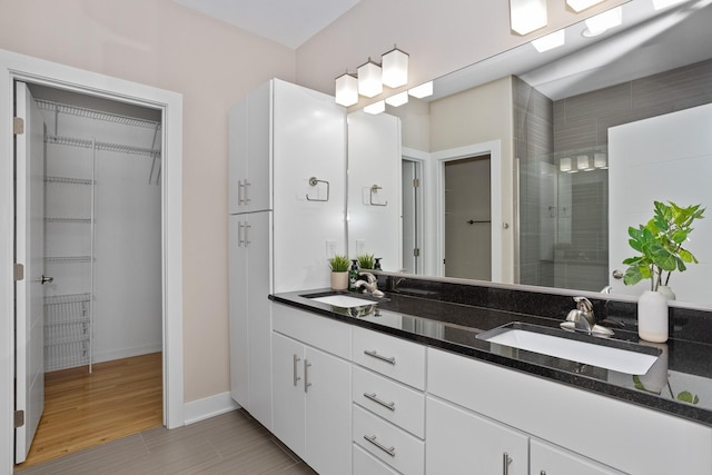 full bathroom with a tile shower, double vanity, a sink, and a walk in closet