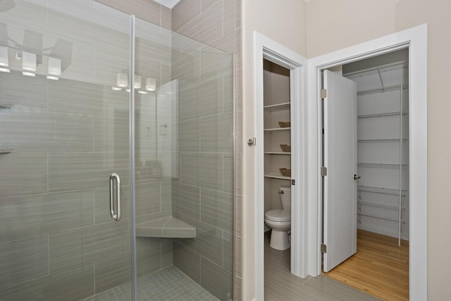 bathroom featuring a stall shower, a spacious closet, toilet, and wood finished floors