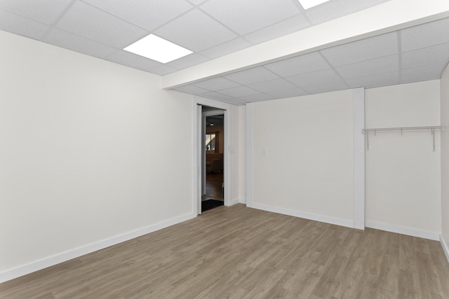 finished basement featuring baseboards, a paneled ceiling, and light wood-style floors