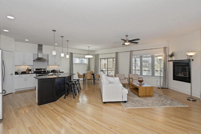 living room with recessed lighting, a glass covered fireplace, ceiling fan, light wood-type flooring, and baseboards