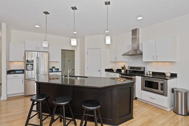 kitchen with a breakfast bar, appliances with stainless steel finishes, light wood-style floors, a sink, and wall chimney range hood