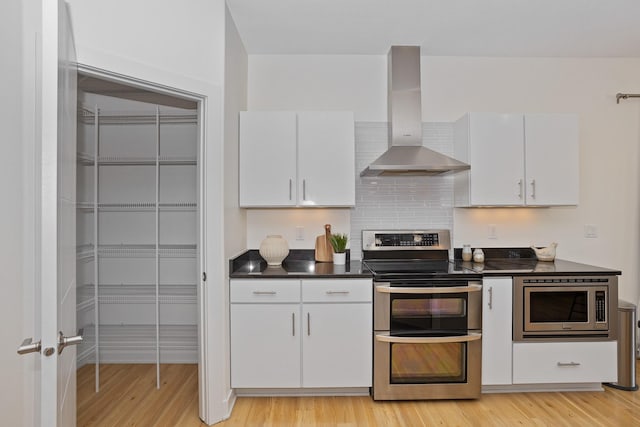 kitchen featuring wall chimney exhaust hood, light wood-style floors, dark countertops, and stainless steel appliances