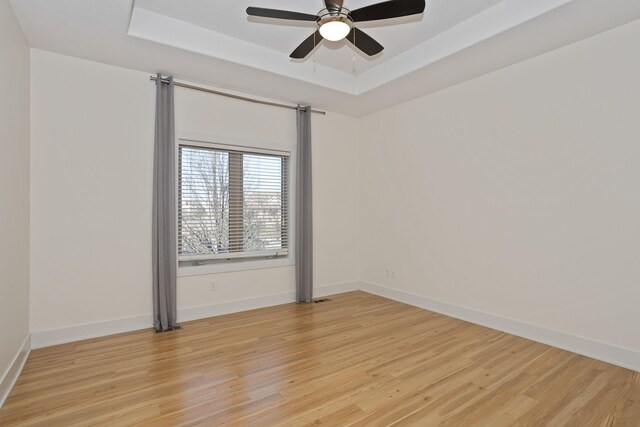 unfurnished room featuring light wood finished floors, baseboards, and a raised ceiling