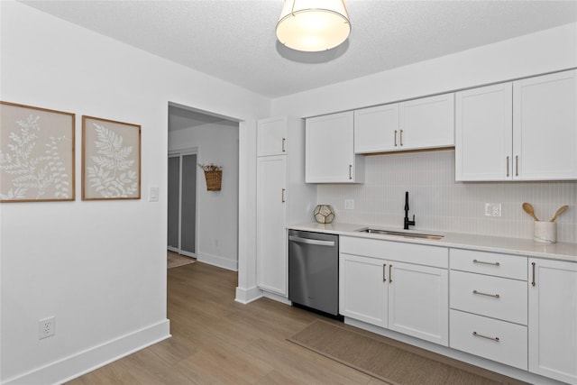 kitchen featuring light countertops, stainless steel dishwasher, white cabinets, a sink, and light wood-type flooring