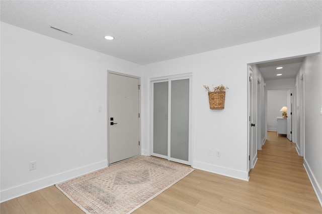 interior space with a textured ceiling, light wood finished floors, visible vents, and baseboards