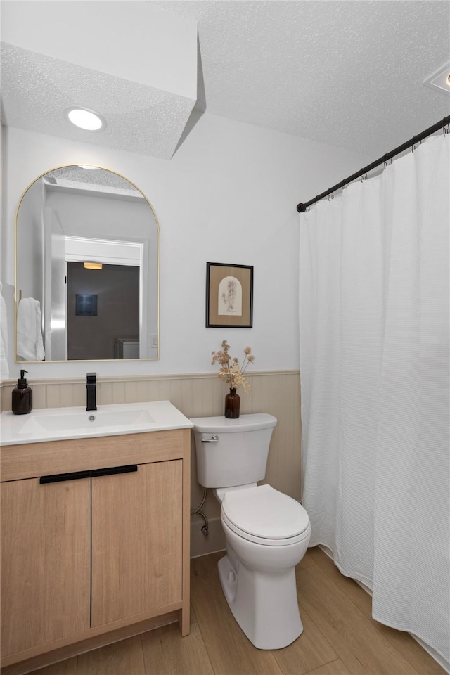 full bathroom featuring toilet, a wainscoted wall, a textured ceiling, and wood finished floors