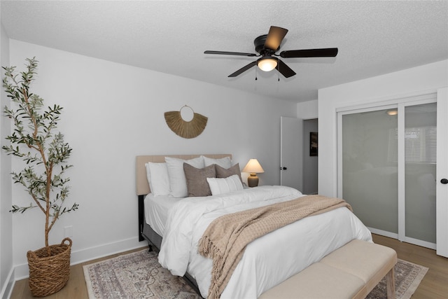 bedroom with a ceiling fan, a textured ceiling, baseboards, and wood finished floors