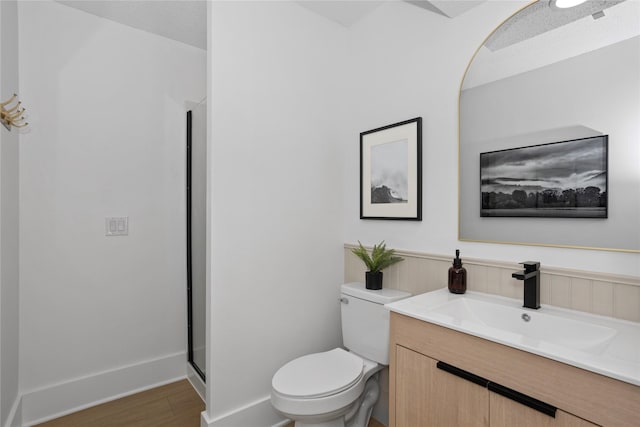 bathroom with a stall shower, vanity, toilet, and wood finished floors