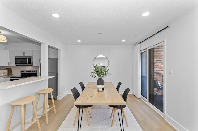 dining space with light wood-style floors, recessed lighting, a textured ceiling, and baseboards