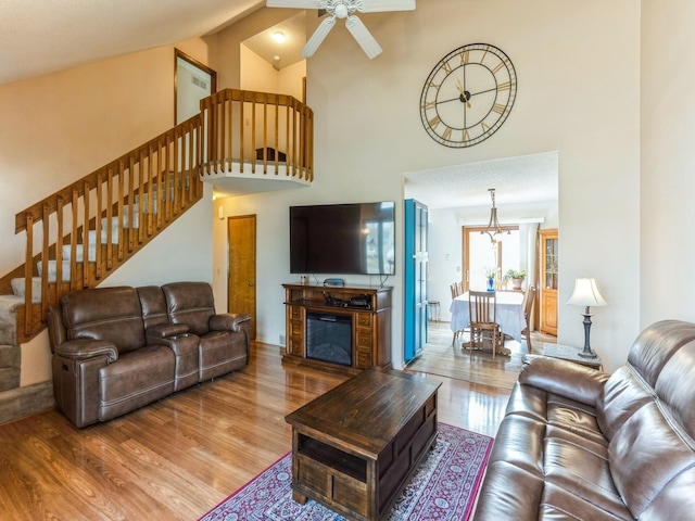 living room with ceiling fan with notable chandelier, high vaulted ceiling, stairway, and wood finished floors