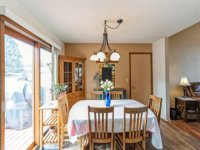 dining space with a textured ceiling, wood finished floors, and a notable chandelier