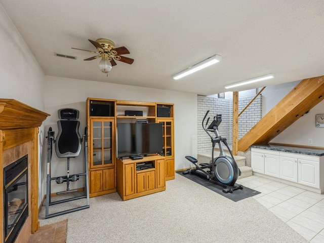 workout room featuring light tile patterned floors, visible vents, a ceiling fan, a glass covered fireplace, and a textured ceiling