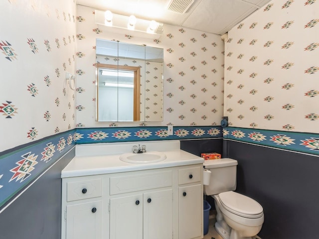 bathroom with toilet, wallpapered walls, visible vents, and vanity