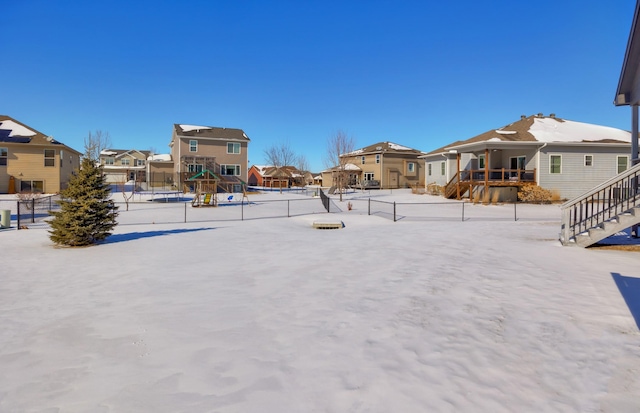 snowy yard featuring a residential view, fence, and playground community