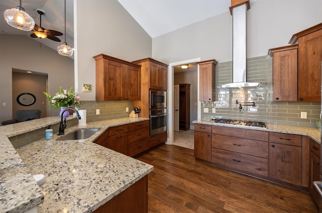 kitchen with stainless steel appliances, wall chimney range hood, a sink, and brown cabinets