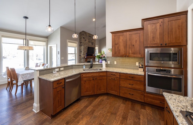 kitchen featuring stainless steel appliances, a peninsula, a sink, dark wood-style floors, and brown cabinetry