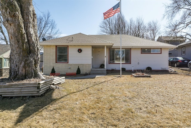 view of front of house with a shingled roof, a front yard, and brick siding