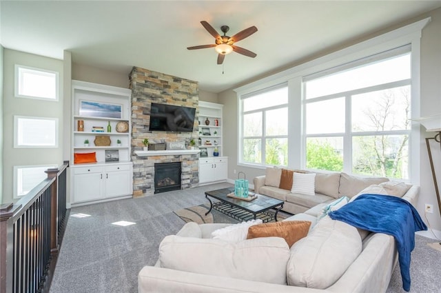 carpeted living area with a stone fireplace, a ceiling fan, and built in features