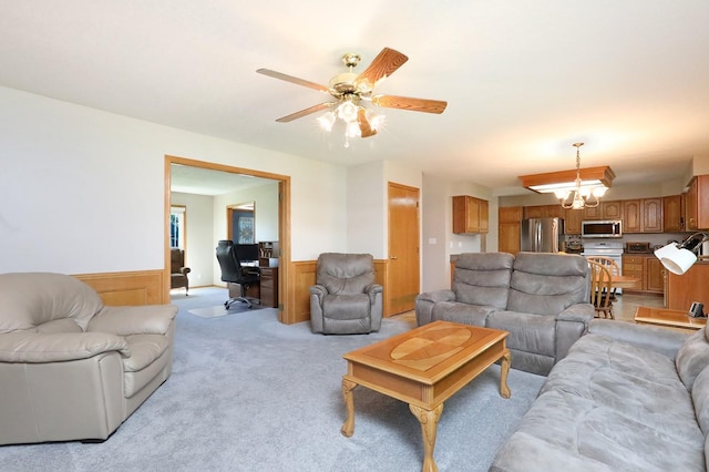 living area with light colored carpet, ceiling fan, and a wainscoted wall